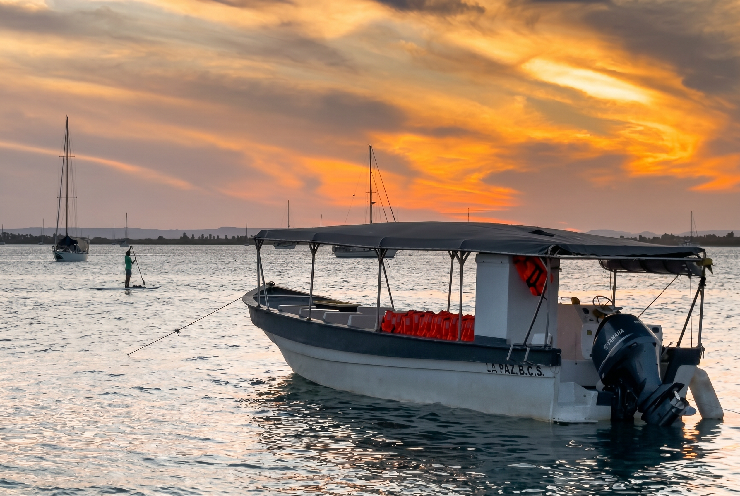 Paddleboarder in the distance behind a moored La Paz panga at sunset